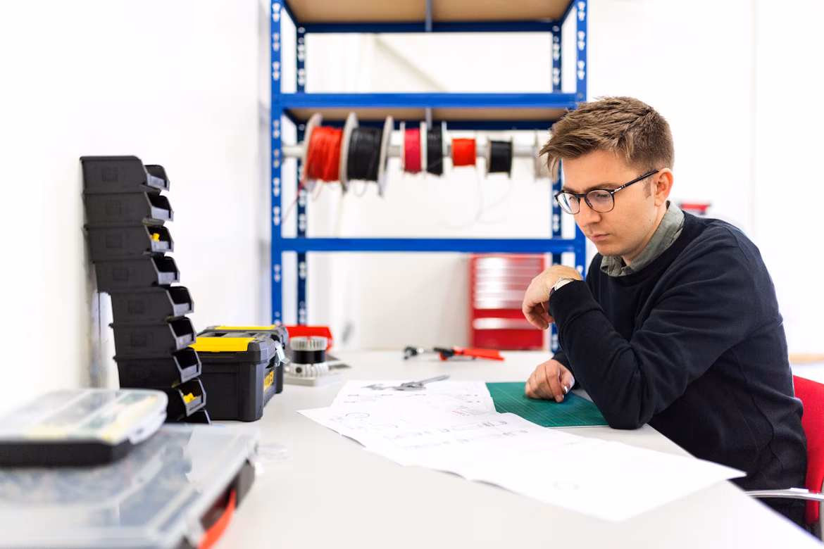A young man sits at a drawing table to look at engineering documents